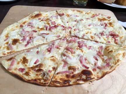 Traditioneller Elsässer Flammkuchen frisch aus dem Ofen – belegt mit Speck, Zwiebeln und Crème fraîche
