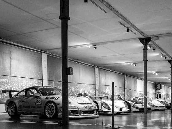 Ausstellungsraum der Cité de l’Automobile in Mulhouse mit historischen Rennwagen, darunter ein Porsche im Vordergrund, schwarz-weiß aufgenommen.