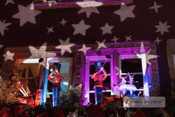 Festlich dekorierte Fensterfront in Riquewihr mit beleuchteten Nussknackern und Sternprojektionen im Advent.